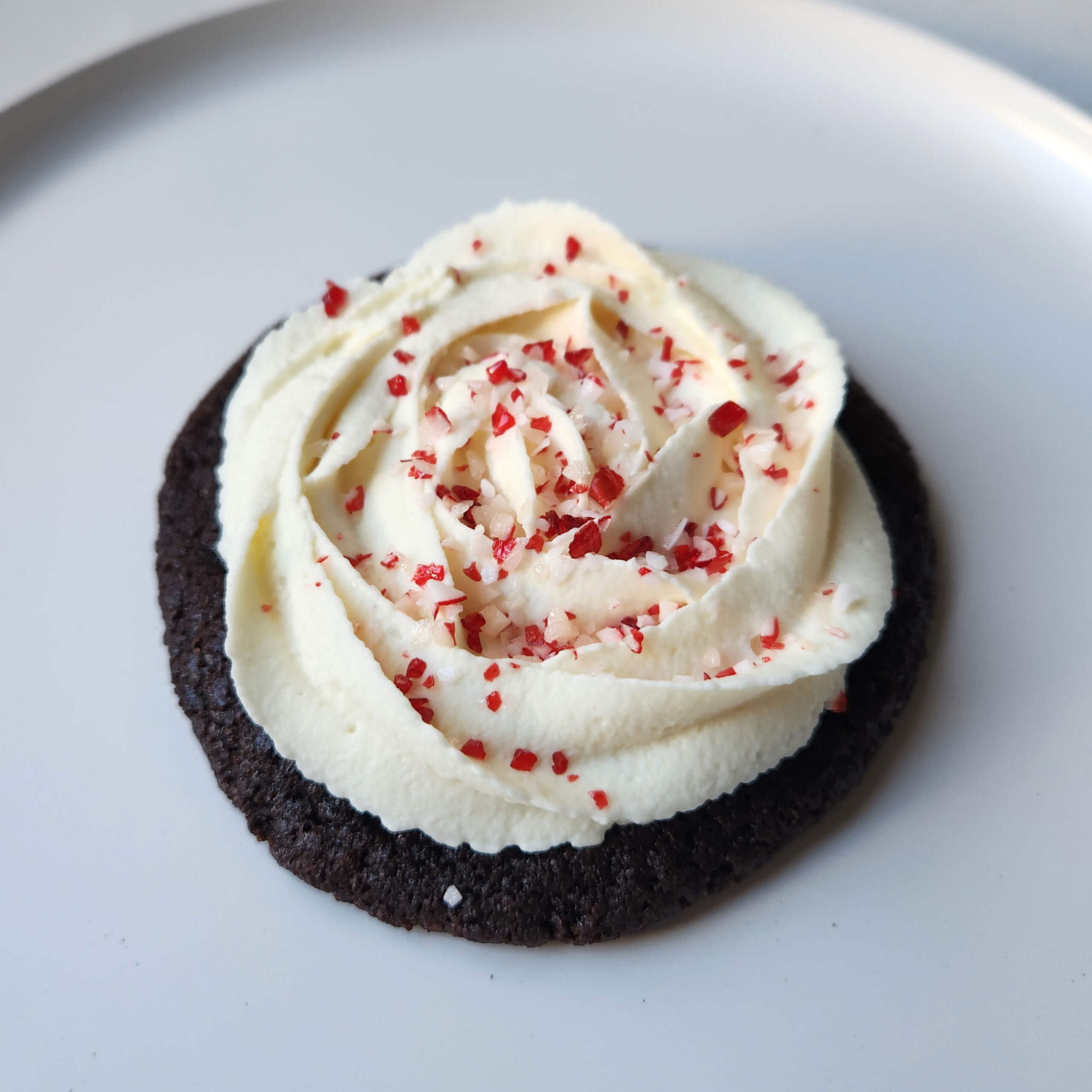 Dark chocolate sugar cookie with peppermint cream cheese buttercream and peppermint candy sprinkle.